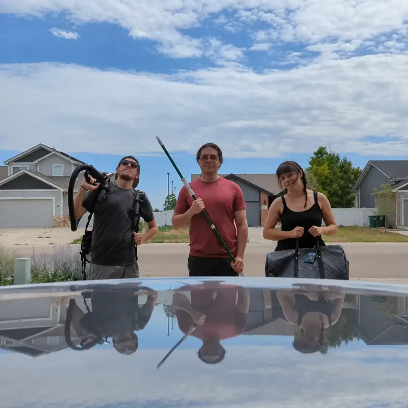 Three Home Cleaning crew members standing in a residential driveway with cleaning equipment and a gear bag